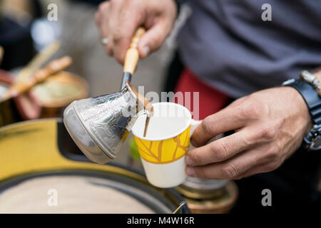 Gros plan des mains de l'homme faire du café turc traditionnel en cuivre turk sur sable chaud fraîchement préparé et verse dans la coupe de papier jetables. Le concept de préparation du café Banque D'Images