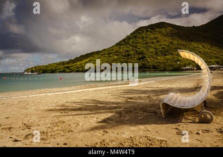 Circulaire original chaise longue sur la plage à St Martin sur un jour nuageux. Un voilier flotte sur l'océan et l'arrière-plan du châssis de green hills. Banque D'Images