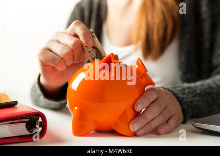 Woman inserting dollar bill dans une tirelire à la maison dans le salon ou bureau Banque D'Images