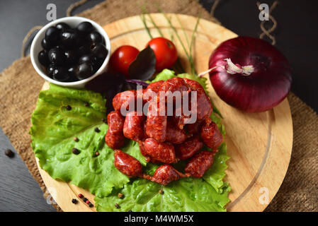 Saucisses de chasse sur une planche en bois avec de la laitue, basilic, tomates cerises, olives et de paprika. Banque D'Images