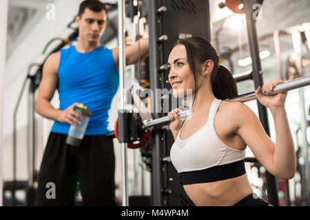 Portrait de belle jeune femme souriant joyeusement tandis que l'entraînement avec haltères longs dans une salle de sport moderne, copy space Banque D'Images