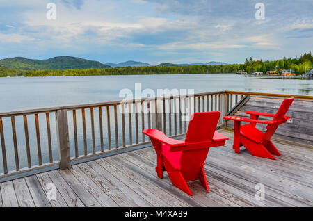 Deux chaises Adirondack rouge vif, reposant sur une terrasse face à l'eau à Lake Placid, New York dans les Adirondacks. Banque D'Images