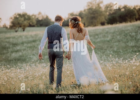 Belle jeune mariée et le marié à l'extérieur dans la nature verte au coucher de soleil romantique. Vue arrière. Banque D'Images