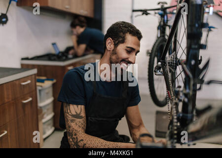 L'homme travaillant sur un vélo dans un atelier de réparation. Sitting fixant une location en atelier. Banque D'Images