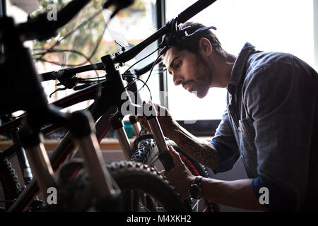 L'inspection d'un mécanicien vélo amortisseurs à l'intérieur d'une montre. L'homme à un vélo d'exposition d'effectuer des réparations. Banque D'Images