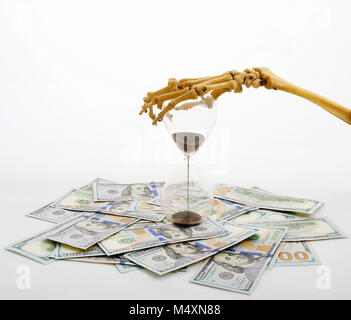 Les doigts de squelette holding sand-verre placé sur dollars. concept de temps - de l'argent et la mort. Banque D'Images