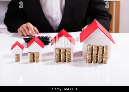 Portrait Of Businessman avec différentes tailles de maisons et des piles de pièces de monnaie avec la calculatrice sur la table Banque D'Images