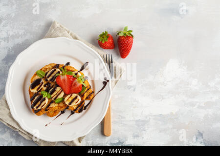 French toasts avec du sirop de chocolat, des fraises et une banane. Fond gris, copie espace, vue du dessus. Banque D'Images