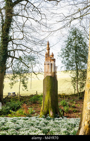 Tapis de perce-neige et de nichoir sculpture d'un château sur la souche d'un arbre mort tronc en bois, Painswick Rococo Garden, Painswick, Glos Banque D'Images