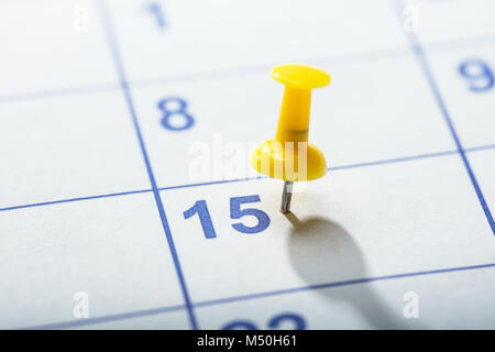 Close-up de punaise jaune collé sur la date dans le calendrier 15e Banque D'Images