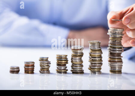 Businessman's Hand de placer la pièce sur le dessus de la pile de pièces Banque D'Images