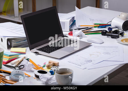 Un ordinateur portable sur le bureau malpropre avec tasse de café et des documents sur le lieu de travail Banque D'Images