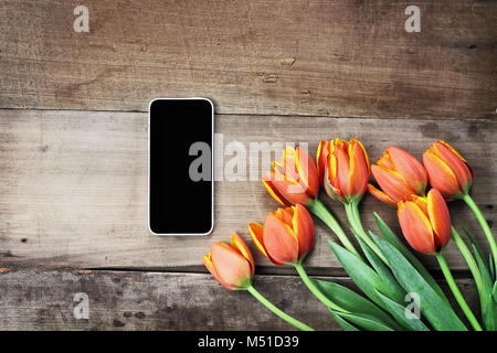 Passage tourné une cellule vide téléphone avec un bouquet de tulipes orange et jaune sur une table en bois. Télévision jeter dessus style. Banque D'Images