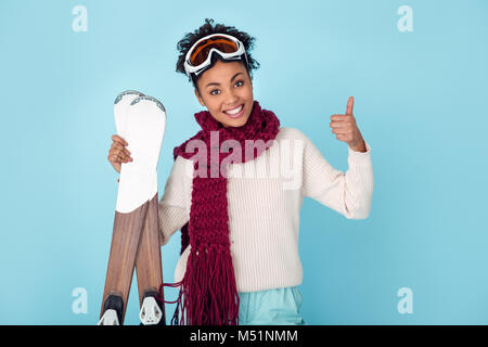 Jeune femme africaine isolé sur mur bleu hiver studio ski thumb up Banque D'Images