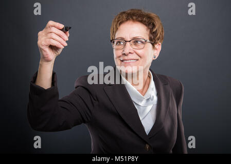 Business senior dame écriture avec marqueur noir et souriant sur fond noir Banque D'Images