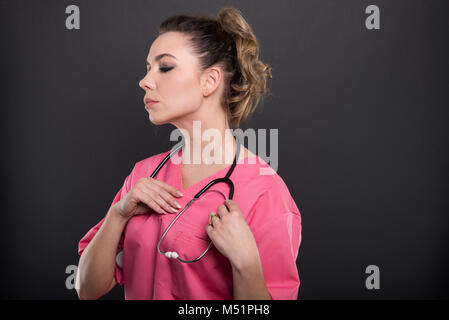 Magnifique Portrait de jeune médecin organiser son stéthoscope sur fond noir avec copyspace zone publicitaire Banque D'Images