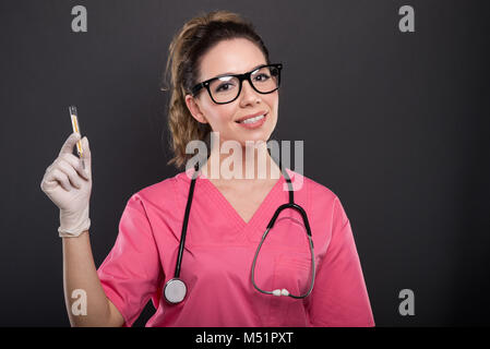 Magnifique Portrait de jeune médecin thermomètre holding et souriant sur fond noir avec copypsace zone publicitaire Banque D'Images