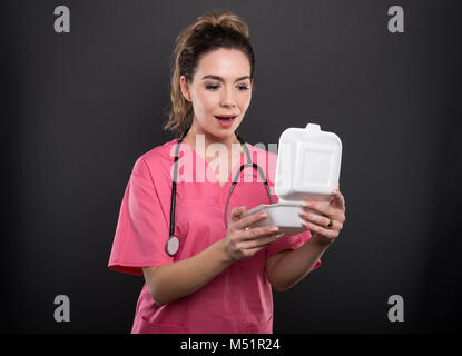 Magnifique Portrait de jeune médecin ouverture lunch box à la surprise sur fond noir Banque D'Images