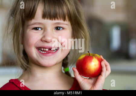 Une jolie petite fille de papier frisé sourit et est titulaire d'une pomme rouge. Portrait d'un bébé heureux de manger une pomme rouge. L'enfant perd des dents de lait. L'alimentation saine Banque D'Images