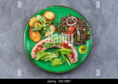 France La saucisse de Toulouse grillée avec potatoaes rôti et salade et lentilles sur fond gris Banque D'Images