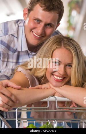 Jeune couple hugging at supermarket - et s'appuyant sur chariot Banque D'Images