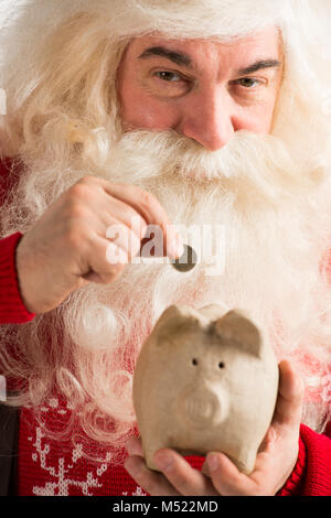 Authentic Santa Claus holding piggy bank et mettre à l'intérieur de pièce d'or, Noël concept budgétaire Banque D'Images