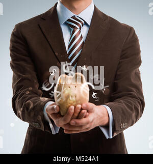 Business man holding piggy bank, symboles de devises volant autour d'elle Banque D'Images