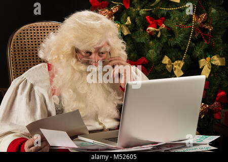 Santa Claus travaillant sur ordinateur la lecture de courriers électroniques et papier lettres des enfants du monde entier Banque D'Images