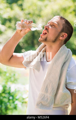 Remise en forme Sport homme. Jeune homme athlétique lui-même après la formation de refroidissement par eau éjacule sur lui-même à partir d'une bouteille de boissons en plein air au parc Banque D'Images