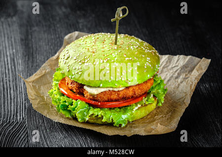 Burger vert escalope de poisson et les tomates. Fond de bois noir Banque D'Images