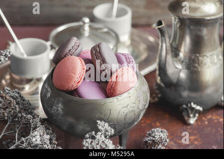 Des petits macarons sur plaque de métal avec de petites fleurs blanches et de thé composition appareils sur fond de bois. Focus sélectif. Banque D'Images