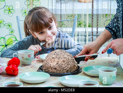 La petite fille attend avec intérêt que mom coupe un délicieux gâteau. Banque D'Images