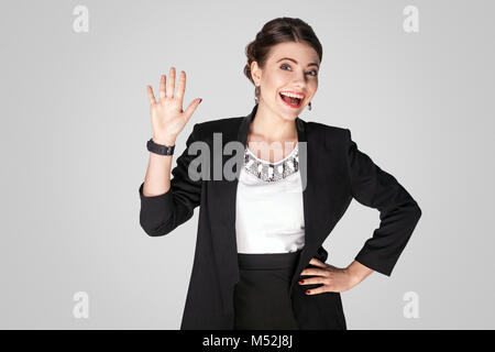 Bien bonjour ! Woman in suit looking at camera et montrant bonjour signe. Studio shot, piscine. Isolé sur fond gris Banque D'Images