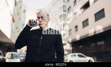 Jeune homme à l'aide de la cigarette électronique pour fumer dans les lieux publics.restriction fumée,interdiction de fumer.En utilisant l'appareil avec des liquides aromatisés vaping.E-juice vaping. Banque D'Images