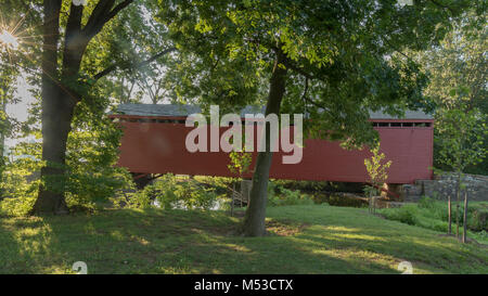 Le soleil forme un starbust culotte throuhg teee les feuilles à la loy's Station pont couvert près de Thurmont MD. Les travées du pont en bois rouge d'un flux au cours de la Banque D'Images