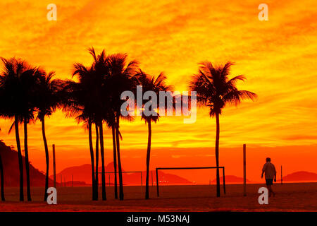 Homme marchant près de quelques arbres de noix de coco à la plage de Copacabana, au lever du soleil, Rio de Janeiro, Brésil Banque D'Images