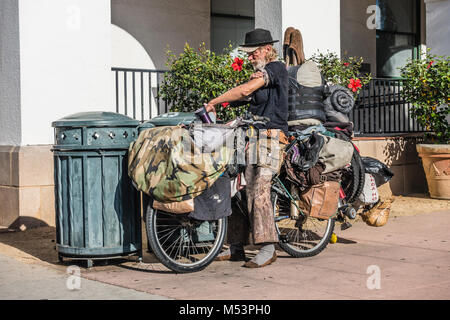 Un homme sans-abri sur son vélo chargé avec ses possessions en scrounging est trash et bacs de recyclage devant l'Hôtel de Ville à Santa Barbara, Cal Banque D'Images