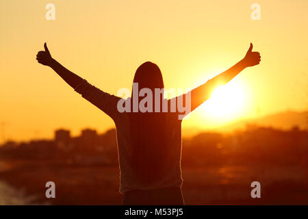 Vue Arrière rétro-éclairage silhouette d'une femme raising arms with Thumbs up au soleil au coucher du soleil Banque D'Images