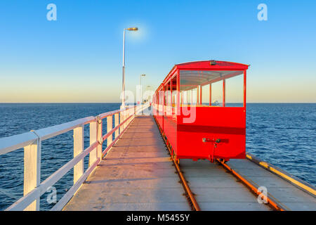 Vue de derrière de vintage train rouge éclairé par le coucher du soleil, la lumière jetée sur les pistes dans la ville de Busselton Busselton, WA. Busselton Jetty est la plus longue jetée en bois dans le monde et emblématiques du lieu. Banque D'Images