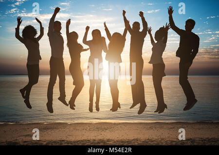 Silhouette de personnes sautant ensemble sur la plage pendant le coucher du soleil Banque D'Images