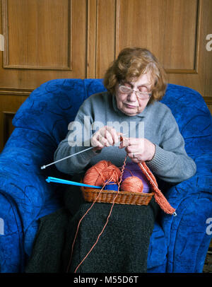 La vieille femme est assise dans un fauteuil knitting Banque D'Images