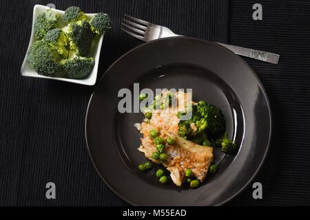 Vue du haut vers le bas de la portion du poisson frit avec des petits pois et les brocolis sur la plaque noire. Éléments nutritifs à faible teneur en gras sain plat délicieux Banque D'Images