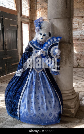 Masque de femme en costume bleu et très décoratif debout à côté de pilier en vieux, salle vide pendant le Carnaval de Venise (Carnaval de Venise). Banque D'Images