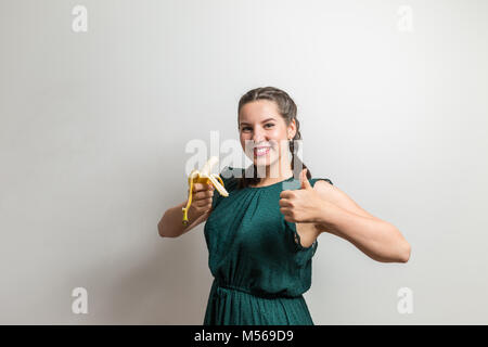 Jolie fille bouclés en robe denim tendance montre un super signe et est titulaire d'banana Banque D'Images