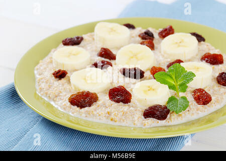 Assiette de porridge d'avoine avec bananes et raisins secs sur place bleu mat - close up Banque D'Images