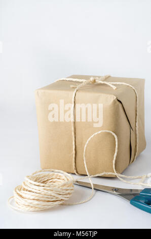 Une parcelle de papier brun lié à un noeud d'une corde. Vestiges de balle string fermé en premier plan avec des ciseaux. Banque D'Images