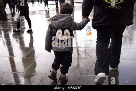 Un jeune garçon tient la main avec un gardien portant un sac à dos pingouin marche à travers les rues humides de Londres. Banque D'Images