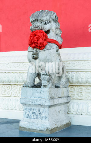 Statue en pierre traditionnelle d'un tuteur chinois lion (femelle), coiffé d'un gros noeud rouge autour du cou pour célébrer le nouvel an chinois, posté à l'avant Banque D'Images