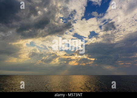 Les rayons du soleil, brisant des nuages orageux dans le ciel bleu au-dessus de l'océan avec la réflexion de l'eau jaune Banque D'Images