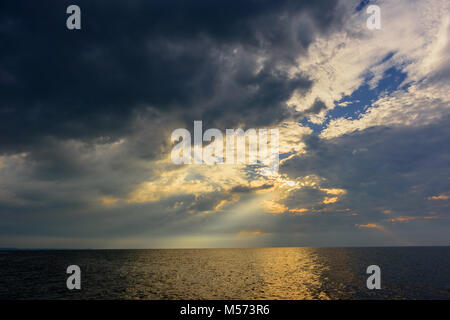 Les rayons du soleil, brisant des nuages orageux dans le ciel bleu au-dessus de l'océan avec la réflexion de l'eau jaune Banque D'Images